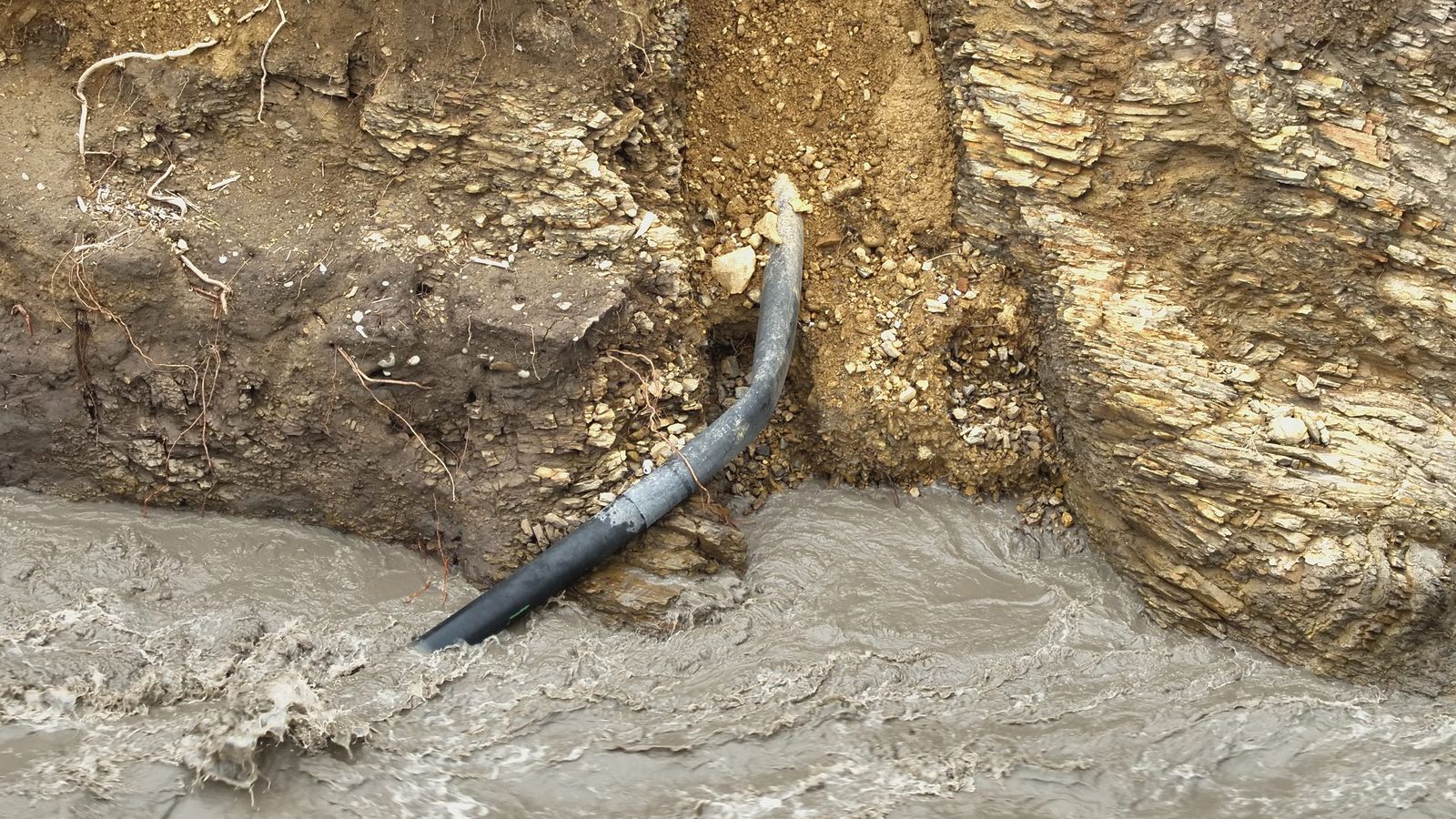 Ducto expuesto y suspendido sobre la margen socavada de un río en crecida